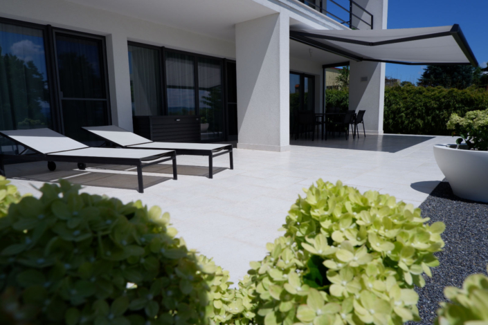 Terrasse Sandro Terrasse in weiß gehalten mit 2 Liegen und Markise, Pflanzen im Vordergrund